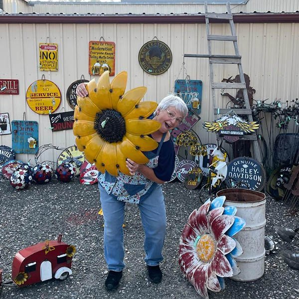 A picture of the owner, Lorena at holding a metal sunflower in front of her store.