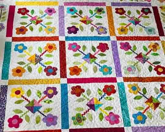 A picture of a quilt with bright flower applique in a grid pattern