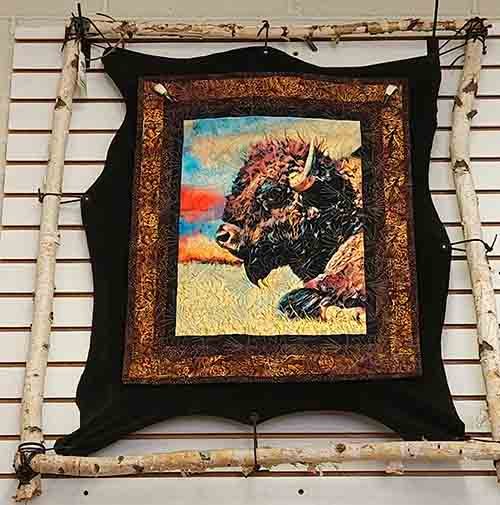 A small quilt with a bison panel attached to a leather back and strapped to a stick frame.