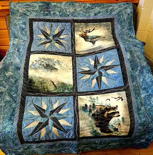 A six block grid quilt with a bear, bird and dear panel along with starburst blocks. Done in blues and greens.